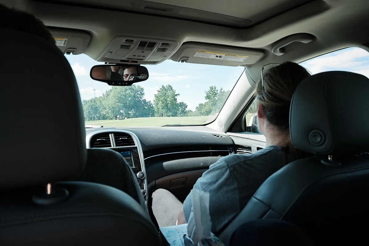 In the back seat of the car looking at my parents in the front seats. You can see me taking the picture in the reflection of the rear-view mirror.