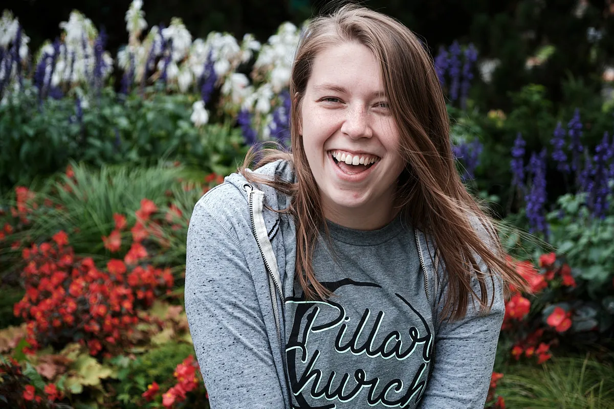 A portrait of Johnna mid-laugh with a vibrant, floral backdrop.