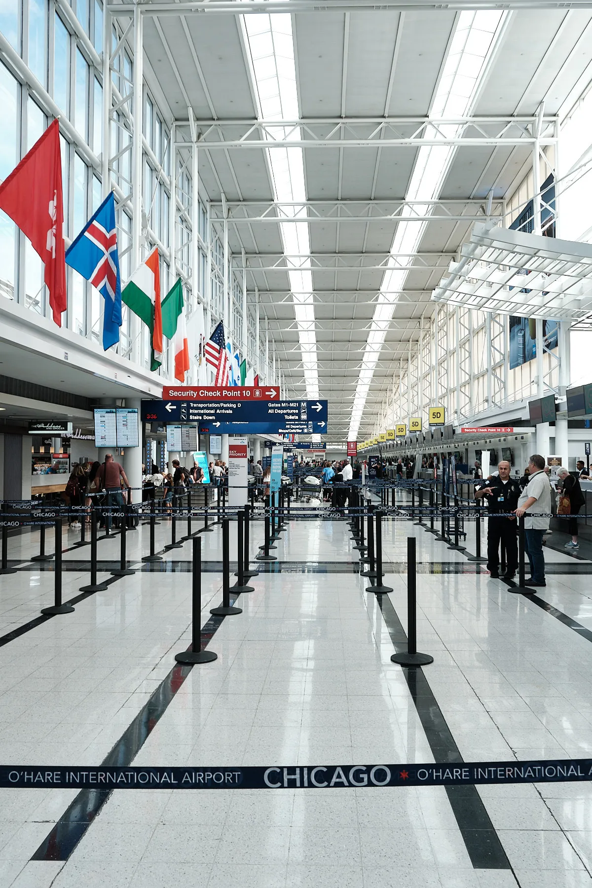 Inside the airport, which isn't very busy, looking down the long foyer where we check in. There are bright windows up high to the left. In front of these windows are many flags from different countries.
