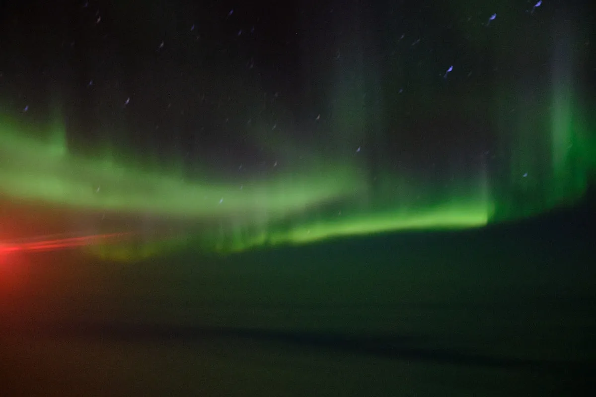 Looking out the plane window high in the air at the green and purple streaks of Aurora Borealis, AKA The Northern Lights. The clouds below the plane are faintly illuminated.