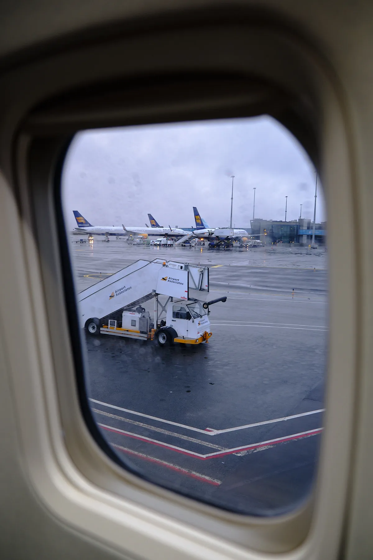 Looking out the plane window, watching a stair car approach the plane as we're parked on the tarmac. We see three other Iceland Air planes parked in the background.